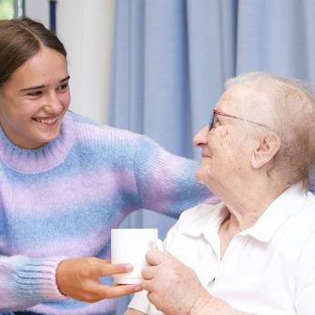 Junge Frau reicht älterer Frau eine Tasse an