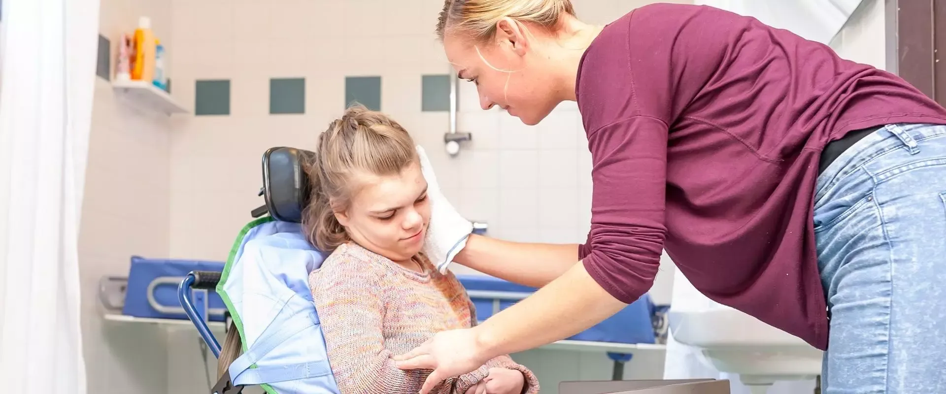 Frau wäscht Kind im Rollstuhl
