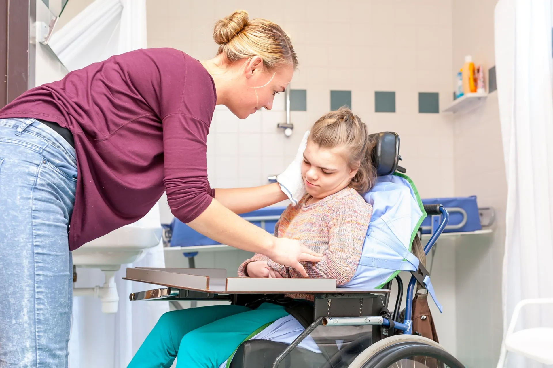 Frau wäscht Kind im Rollstuhl