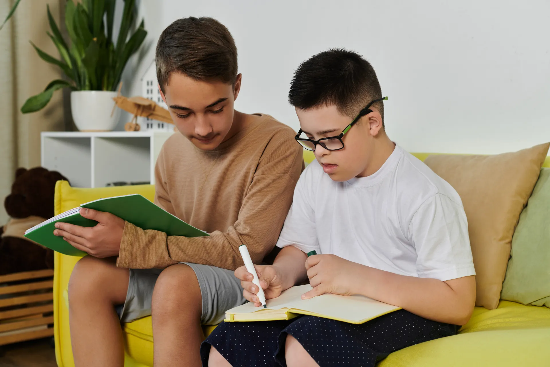 Zwei Brüder sitzen auf der Couch, einer hat das Dwon-Syndrom, der Bruder hilft bei den Hausaufgaben