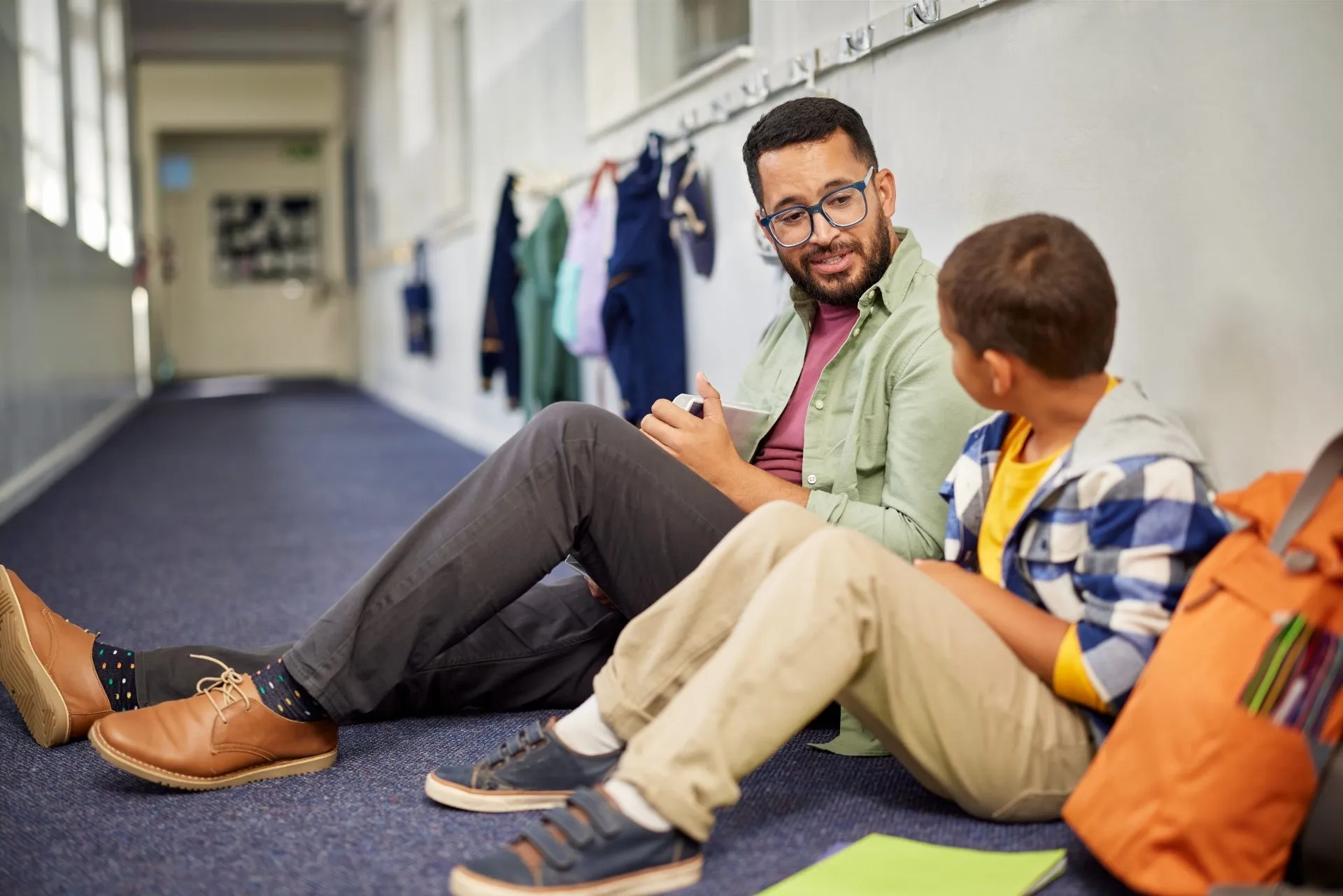 Junger Mann sitzt mit Schüler auf dem Boden im Flur einer Schule