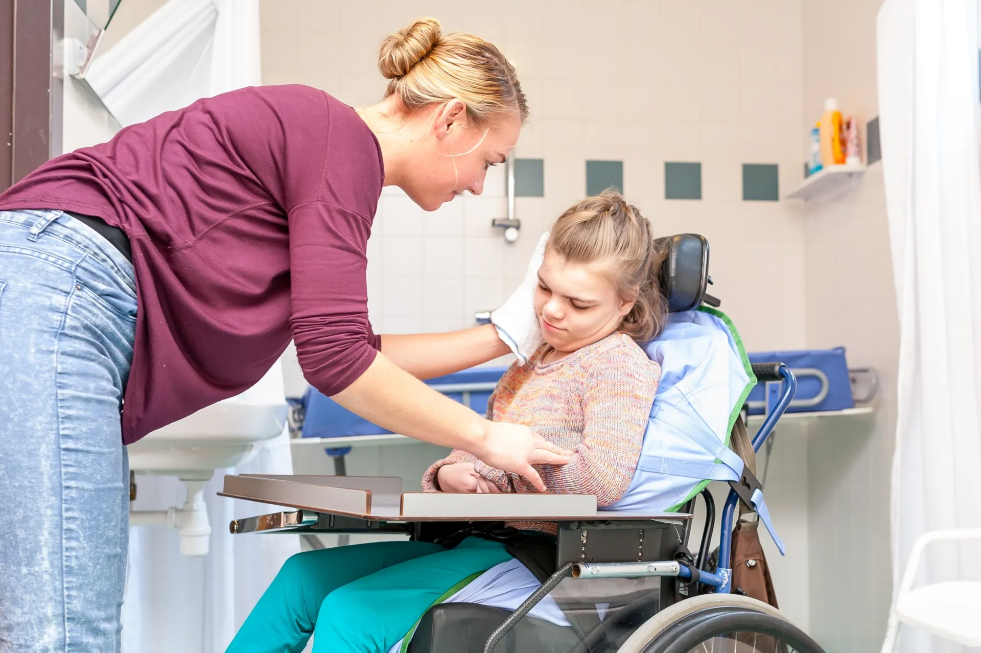 Frau wäscht Kind im Rollstuhl