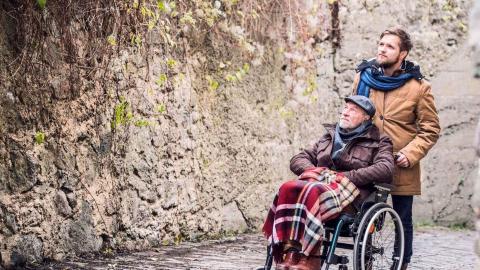Mann schiebt Rentner im Rollstuhl