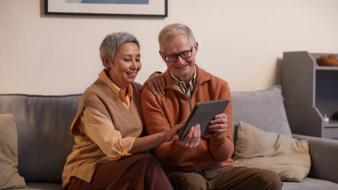 älteres Päärchen sitzt mit einem Tablet auf einem Sofa