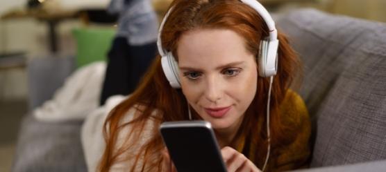 Foto: Frau mit Handy und Kopfhörer auf der Couch