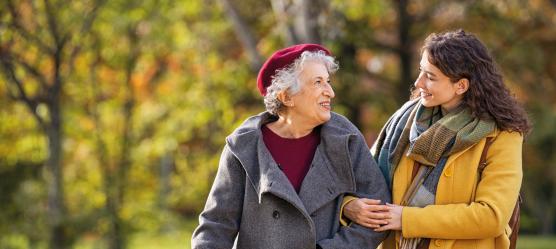 Seniorin und Schwiegertochter spazieren Arm in Arm im Park