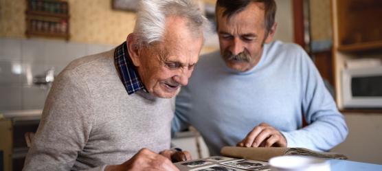 ein ältere Mann guckt mit seinem Sohn ein Fotoalbum in der Küche an