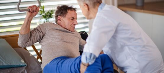 Pflegerin gibt Pflegekurs indem sie angehörigen zeigt wie man einen Pflegebedürftigen Menschen hebt