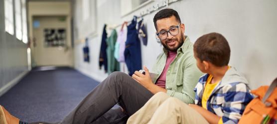 Junger Mann sitzt mit Schüler auf dem Boden im Flur einer Schule
