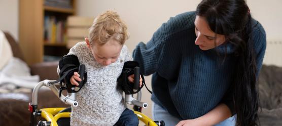Pflegende Mutter und Kind, welches Orthesen trägt und einen Walker nutzt