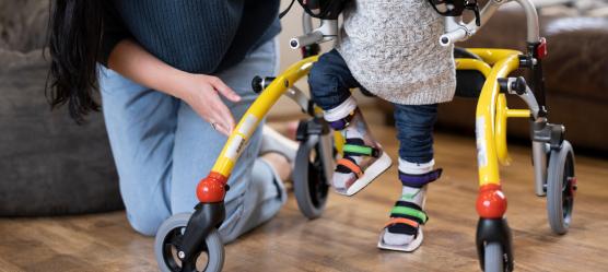 pflegende Mutter mit Kind welches Orthesen trägt und einen Walker nutzt