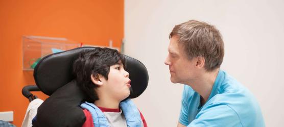 behindertes Kind im Rollstuhl wird von einem Pfleger betreut