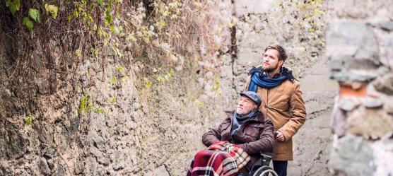 Mann schiebt Rentner im Rollstuhl