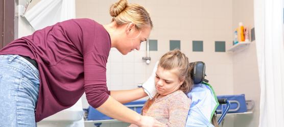 Frau wäscht Kind im Rollstuhl