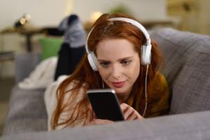 Foto: Frau mit Handy und Kopfhörer auf der Couch