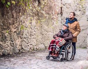 Mann schiebt Rentner im Rollstuhl