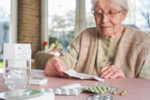 Bild einer alten Dame am Tisch mit Medikamenten